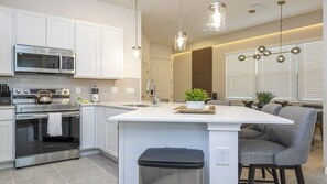A modern kitchen with white cabinetry, stainless steel appliances, and a central island with bar stools. - 5BR Luxury Townhouse with Pool at Paradiso Grande (Orlando)