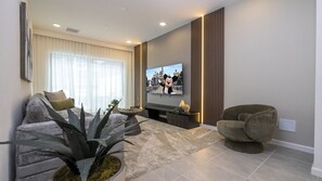 A living room with a flat-screen TV, a sofa, a chair, and a large plant. - 5BR Luxury Townhouse with Pool at Paradiso Grande (Orlando)