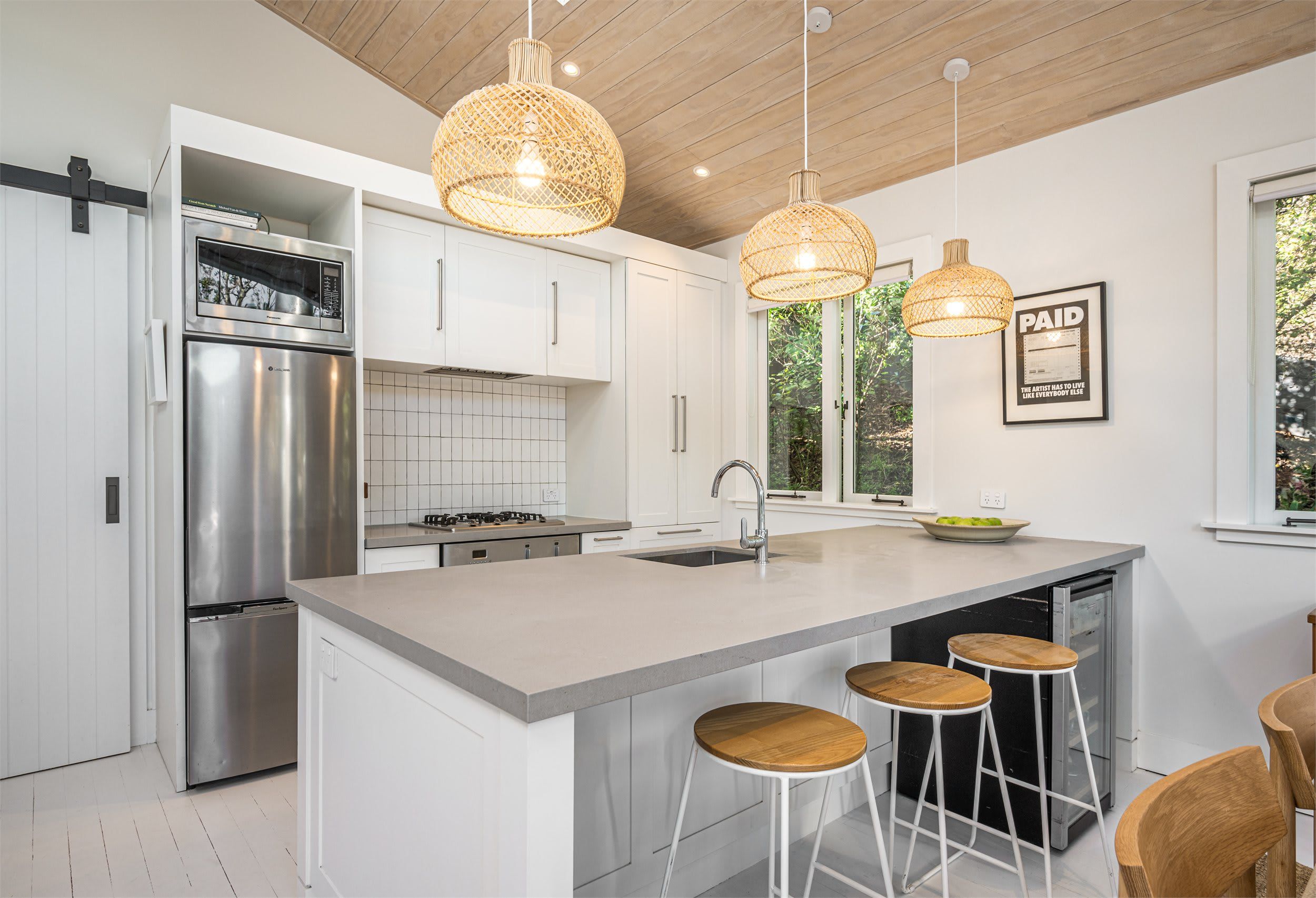 A modern kitchen with white cabinetry, stainless steel appliances, a central island with stools, and pendant lighting.