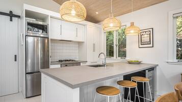 A modern kitchen with white cabinetry, stainless steel appliances, a central island with stools, and pendant lighting.
