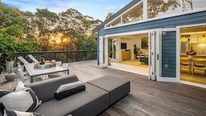 Une terrasse extérieure moderne comprenant un espace repas, un canapé et une cuisine visible à travers une porte ouverte.
