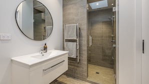 Une salle de bain moderne avec un meuble-lavabo blanc, un miroir rond, une cabine de douche en verre et un porte-serviettes.
