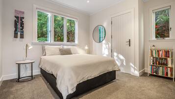 A bedroom with a bed, bedside tables, a bookshelf, and large windows.