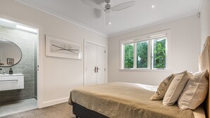 Une chambre à coucher comprenant un lit, une fenêtre, une porte, un ventilateur de plafond, et une salle de bain avec un miroir et un lavabo.