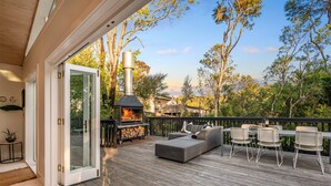 Une terrasse extérieure dotée d’un poêle à bois, d’un espace salon et d’une porte vitrée donnant sur l’intérieur.