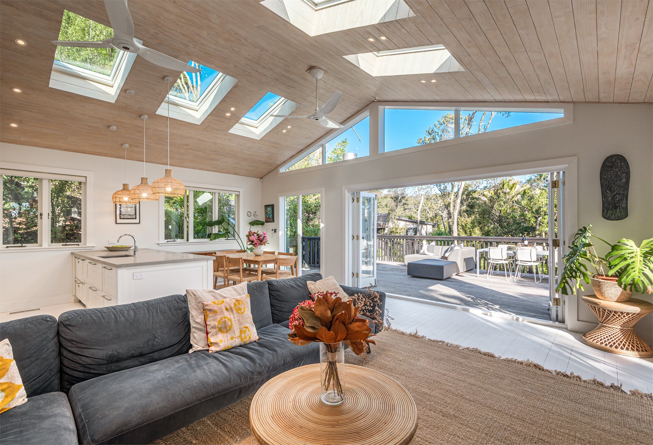A modern living room with a grey sofa, a dining area, and a view of the outdoors through large windows.