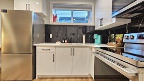 Una cocina moderna con un refrigerador de acero inoxidable, gabinetes blancos, una ventana con persianas y una cafetera sobre la encimera.