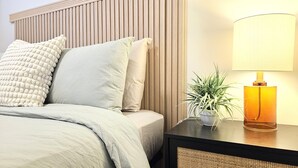 Una cama bien hecha con almohadas, una mesita de noche con lámpara y una planta en maceta.