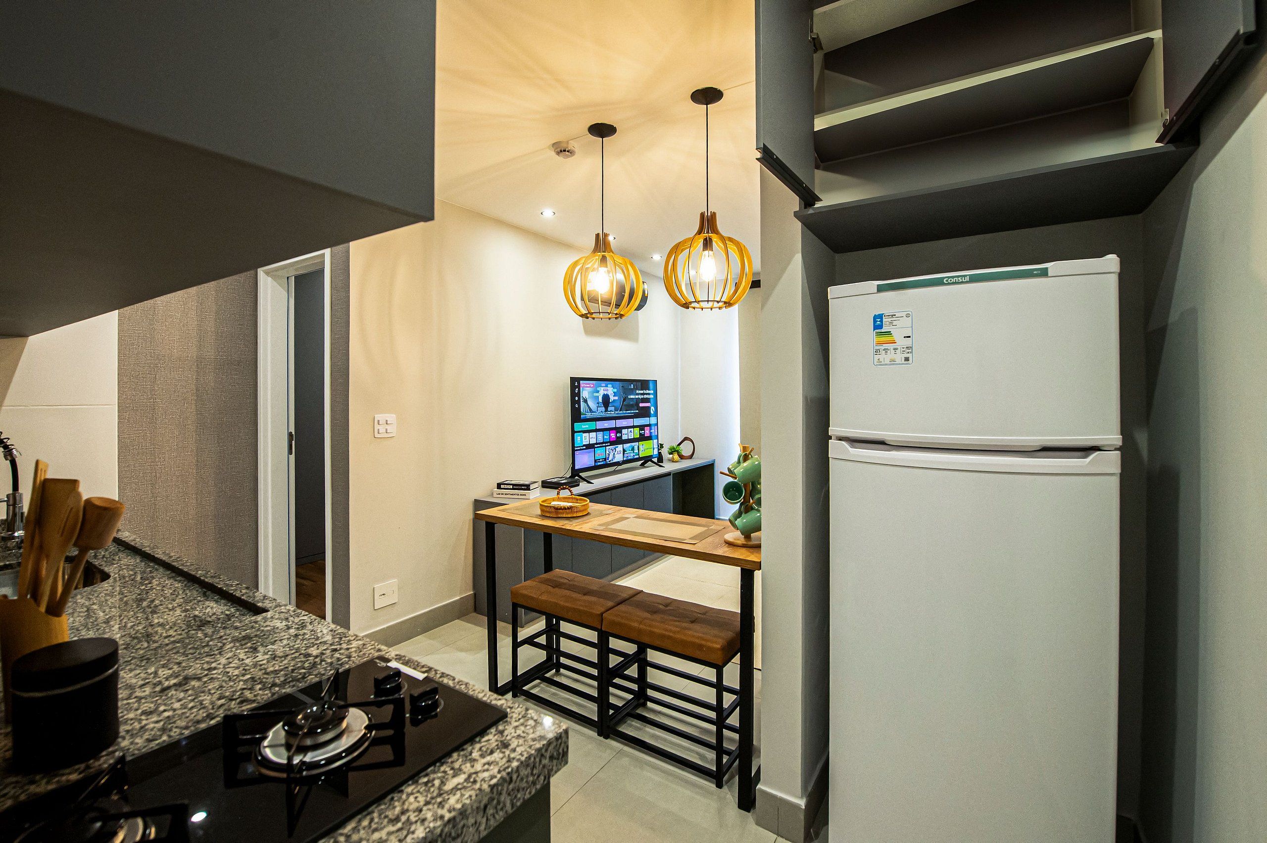 Cocina compacta con estufa a gas integrada, un banco de madera, dos lámparas colgantes y un refrigerador.
