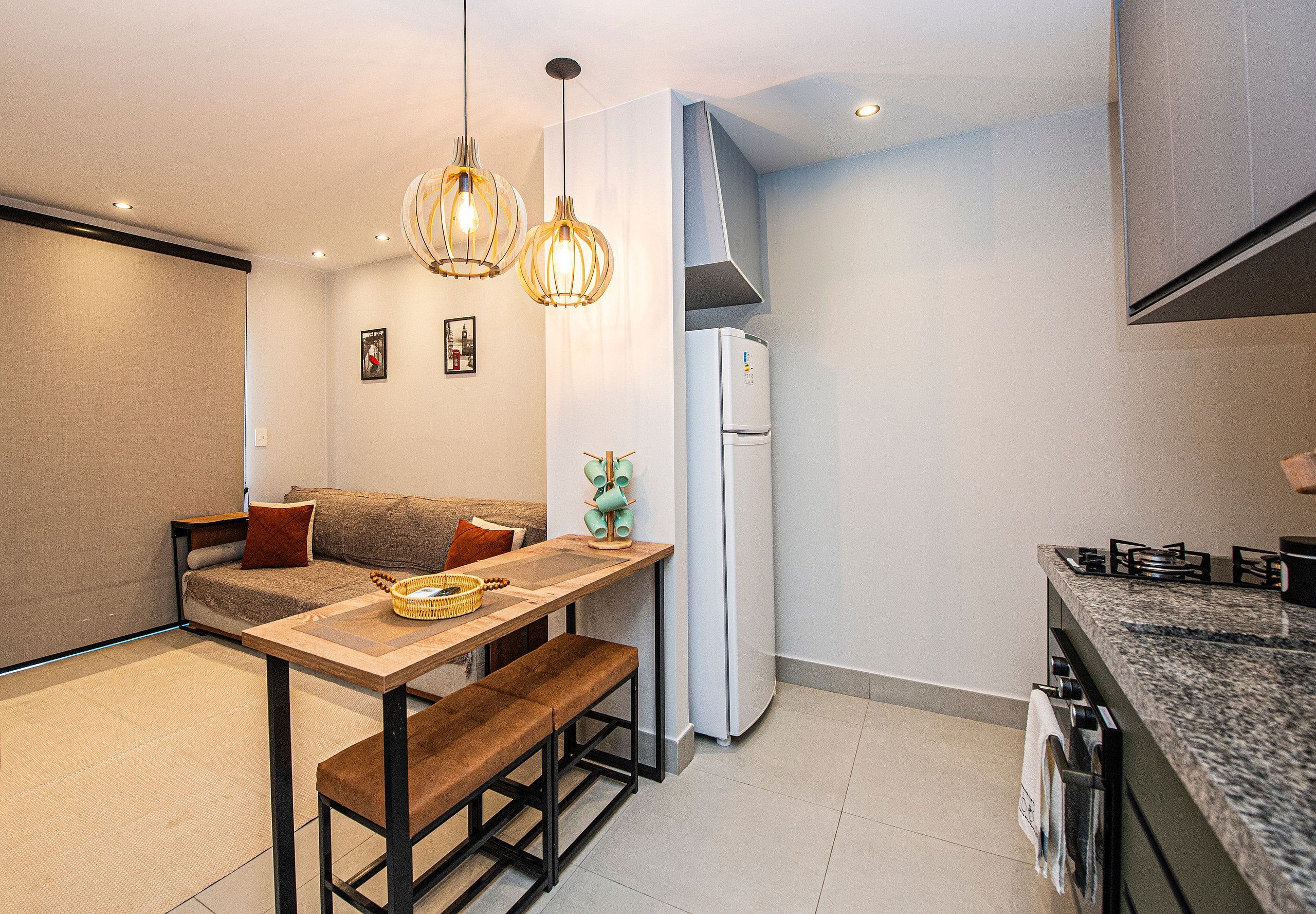 A compact kitchen with a dining area, featuring a wooden table, bench, and hanging pendant lights.