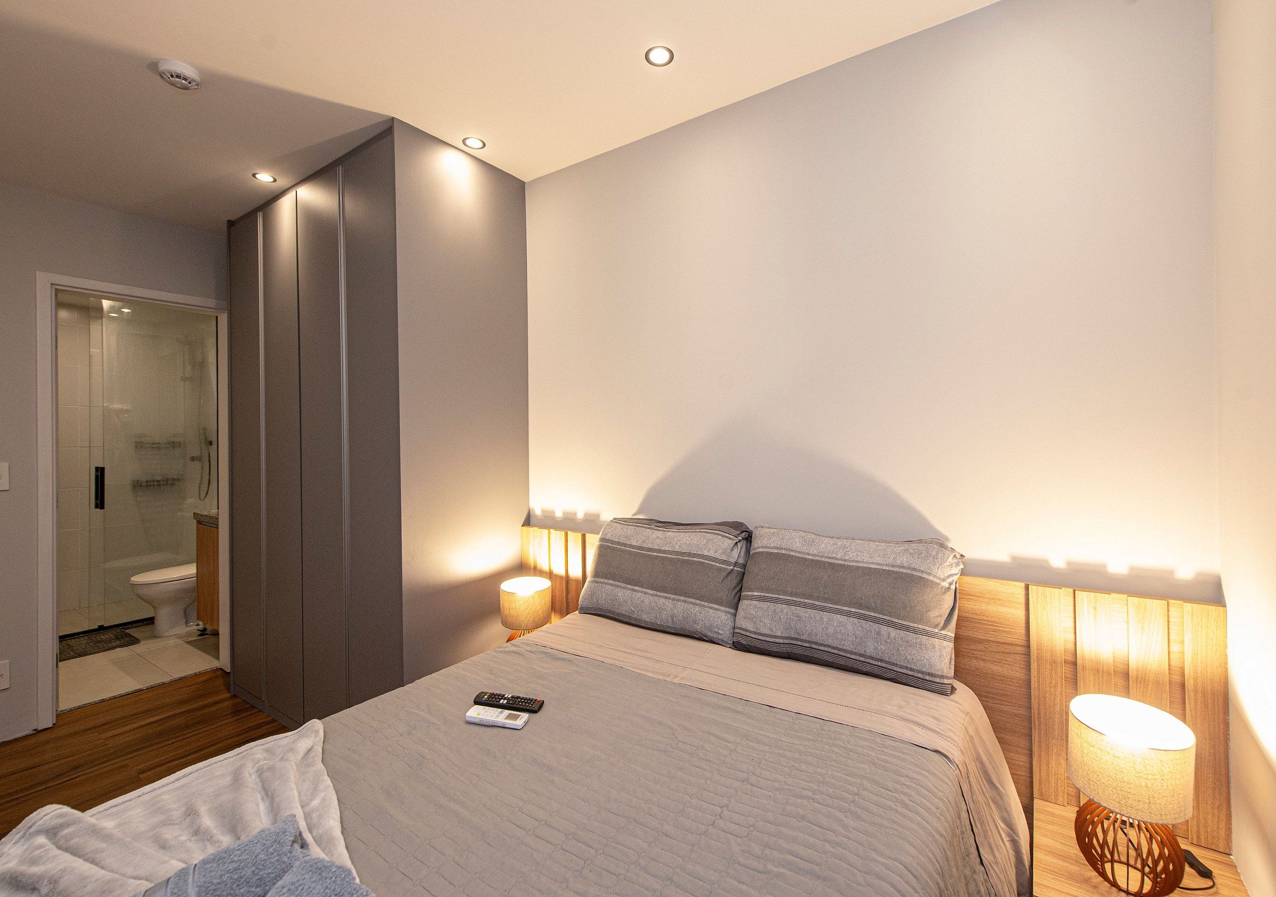 Quarto com cama, abajures, um controle remoto e cabeceira de madeira.