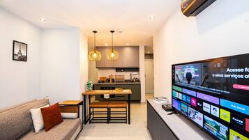 Una sala de estar moderna con un sofá, una mesa de comedor y un televisor que muestra varios canales.