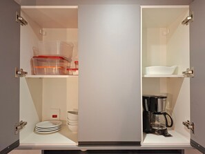 Una cocina con un armario blanco, una cafetera y una pila de platos.