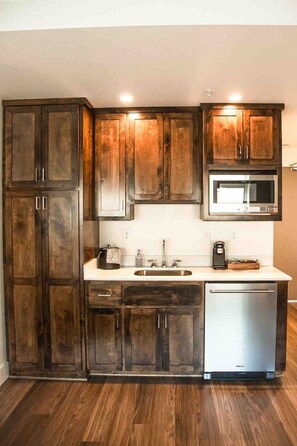 Una cocina con armarios de madera oscura, un lavamanos de acero inoxidable, un microondas y un lavavajillas.