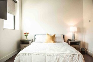 Un dormitorio con una cama, dos mesitas de noche, una lámpara y una ventana.