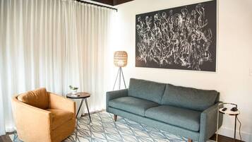 Uma sala de estar com sofá, poltrona, tapete estampado, luminária de chão e uma grande pintura abstrata na parede.
