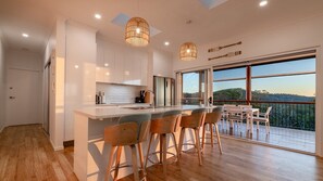 A modern kitchen with a large island, bar stools, and a view of the outdoors. - Dora's Place | Pet Friendly | Sunset Views (Agnes Water)