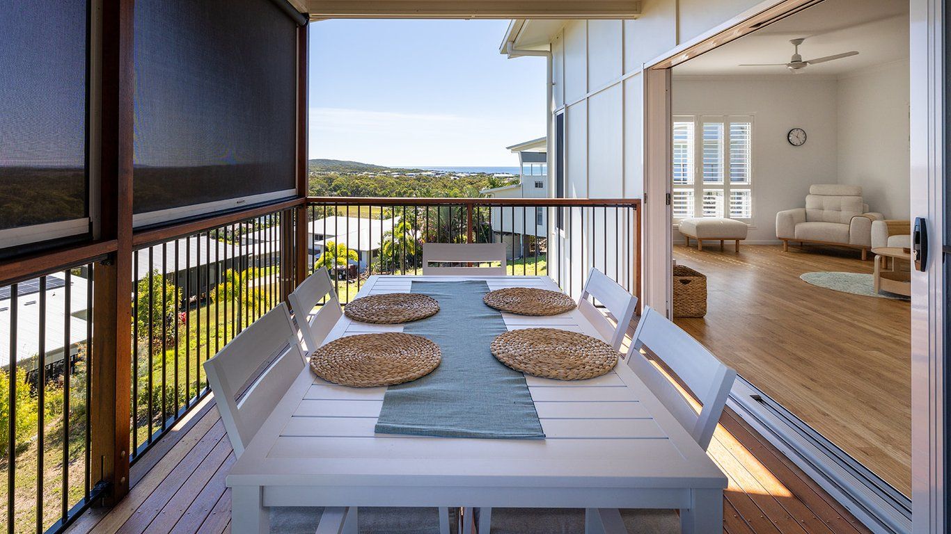 Un balcon avec une table et des chaises, une vue sur le paysage, et une pièce avec un canapé et une horloge.
