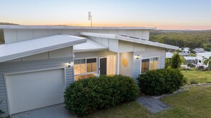 A modern two-story house with a garage, large windows, and a view of the surrounding landscape. - Dora's Place | Pet Friendly | Sunset Views (Agnes Water)
