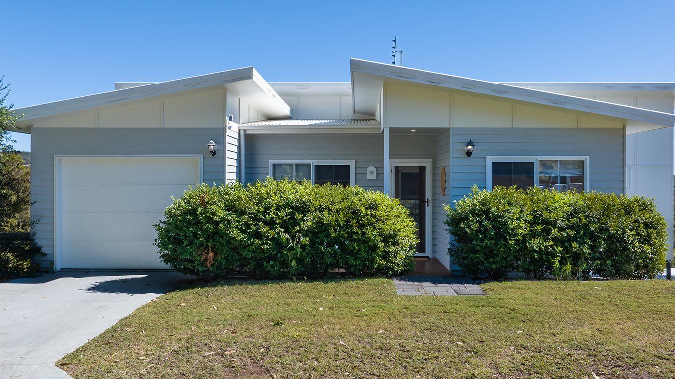 A single-story house with a garage, a covered porch, and two well-maintained bushes in front.