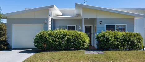 A single-story house with a garage, a covered porch, and two well-maintained bushes in front.
