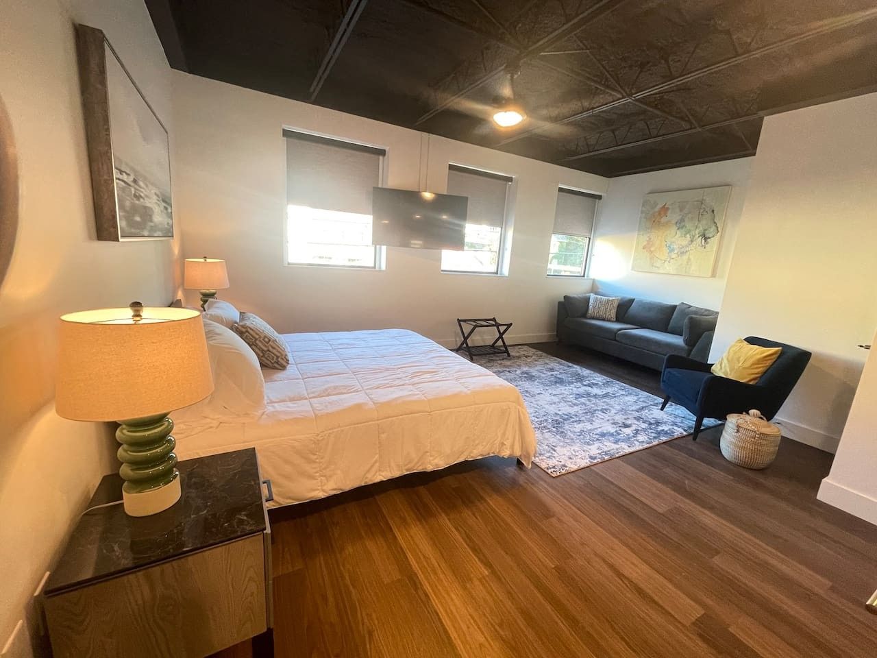 Une chambre à coucher avec un lit, une lampe de chevet, un plancher en bois et un canapé à l’arrière-plan.