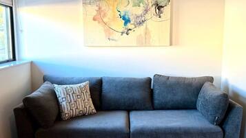 Um sofá cinza com uma almofada estampada em frente a uma parede com um quadro abstrato colorido.