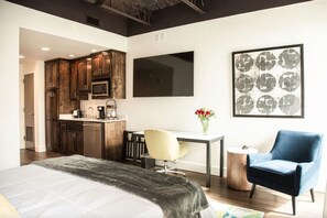 A modern hotel room with a large bed, a desk, a chair, a kitchenette, and a flat-screen TV. - The Lofts Suite #21 `The Judge` King Bed & Balcony (Wetumpka)