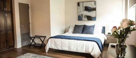 A bedroom with a bed, a nightstand, a vase with flowers, and a painting on the wall.