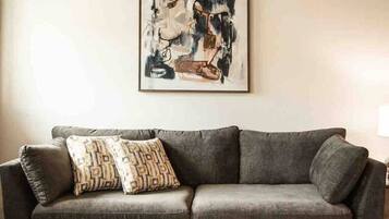 Sala de estar com um sofá cinzento, uma almofada decorativa estampada e uma grande pintura abstrata na parede.