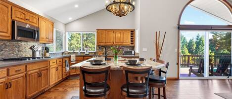 A spacious kitchen with wooden cabinets, a central island with bar stools, a stainless steel oven, and a large window providing natural light.