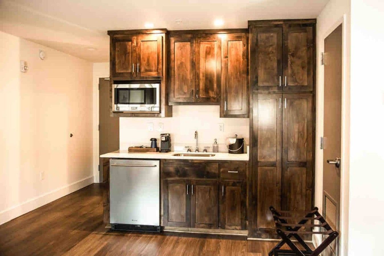 A compact kitchen with wooden cabinets, a stainless steel refrigerator, a microwave, and a dishwasher.