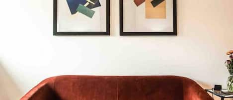 A red sofa in a room with two abstract paintings on the wall.