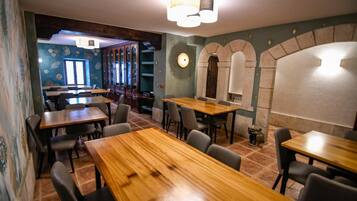 Interior de restaurante con mesas y sillas de madera, pared azul con motivos decorativos y un arco de piedra.