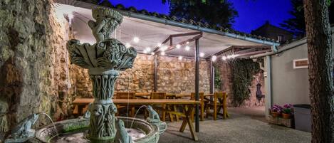 An outdoor patio area with stone walls, a fountain, and a covered seating area.