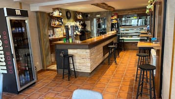 Zona de bar con taburetes, un refrigerador lleno de bebidas y una barra con cafetera.