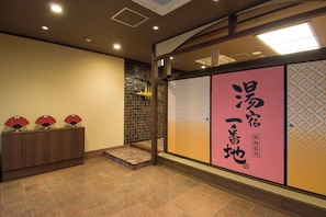 A reception area with a wooden desk, a tiled floor, and a wall with a decorative panel and Japanese calligraphy. - atamionsen yuyadoichibanchi (Atami)