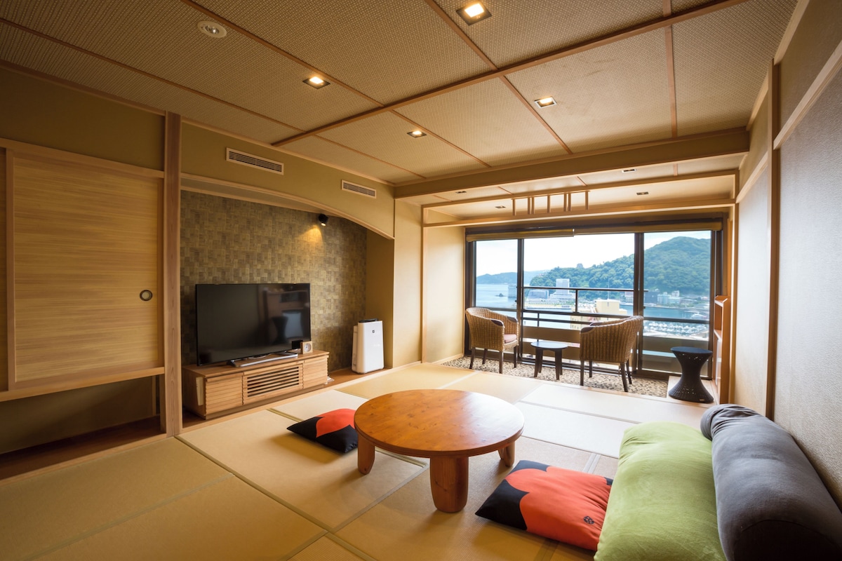 A traditional Japanese-style living room with tatami flooring, a low wooden table, a sofa, and a television.