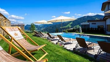 Ein Poolbereich mit Liegestühlen und Sonnenschirmen, eine Steinmauer und Blick auf Berge.