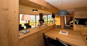 Interior em madeira com área de jantar, cozinha e uma janela grande.