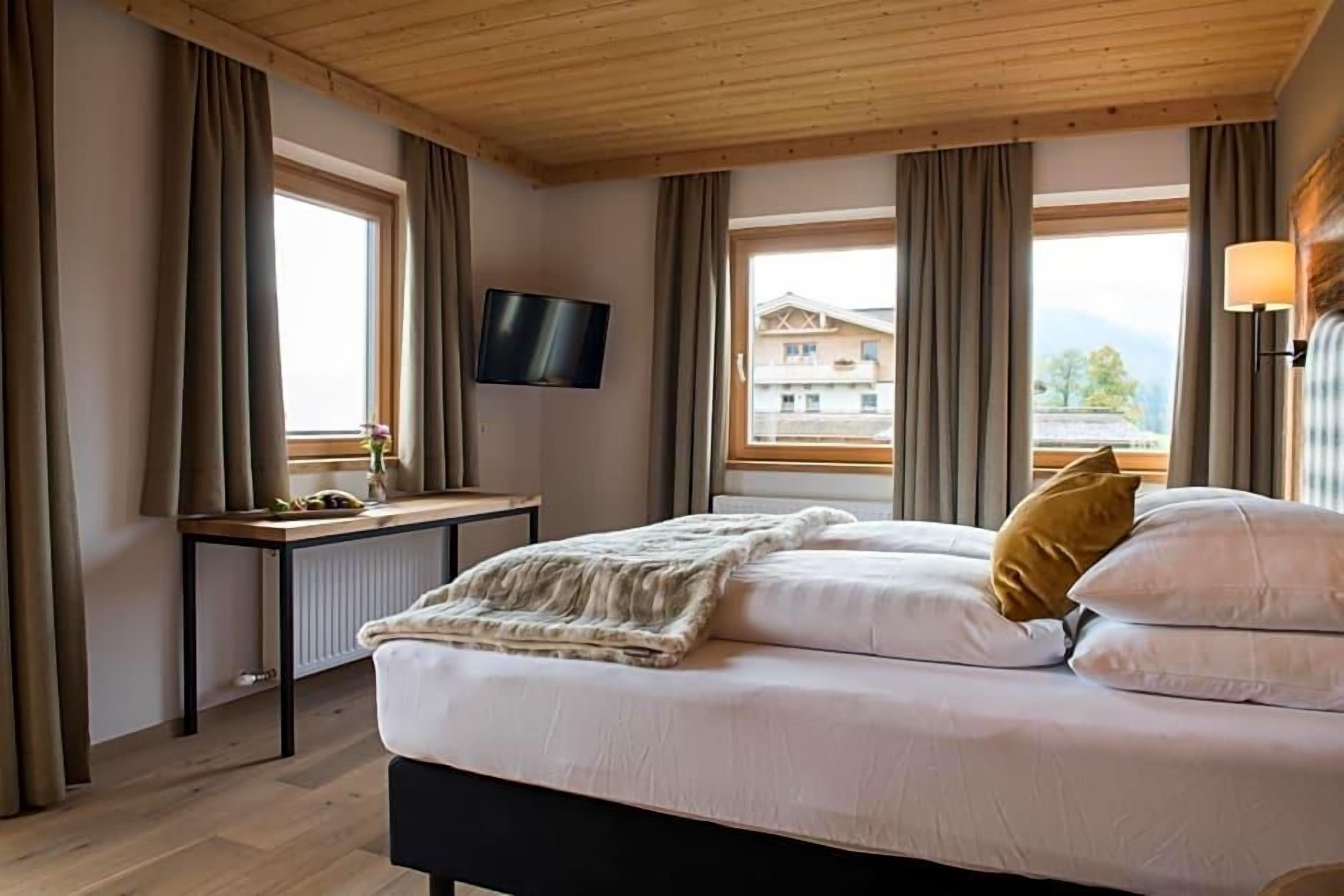 Ein Schlafzimmer mit einem Bett, einem Schreibtisch, einem Fernseher und einem Fenster mit Vorhängen.