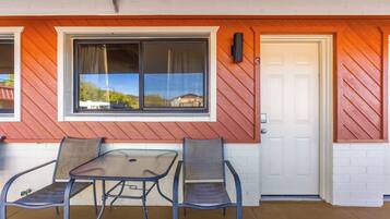 A covered patio with a table and two chairs, a white door, and a window with a view of houses.