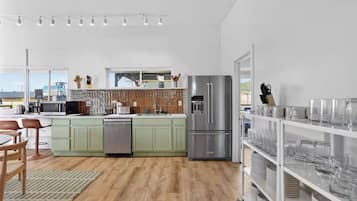 Una cocina moderna con un refrigerador de acero inoxidable, un lavavajillas y un microondas. Hay un comedor con una mesa y sillas.