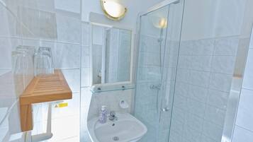 Un baño con cabina de ducha de vidrio, un lavamanos con espejo y un estante de madera con vasos.