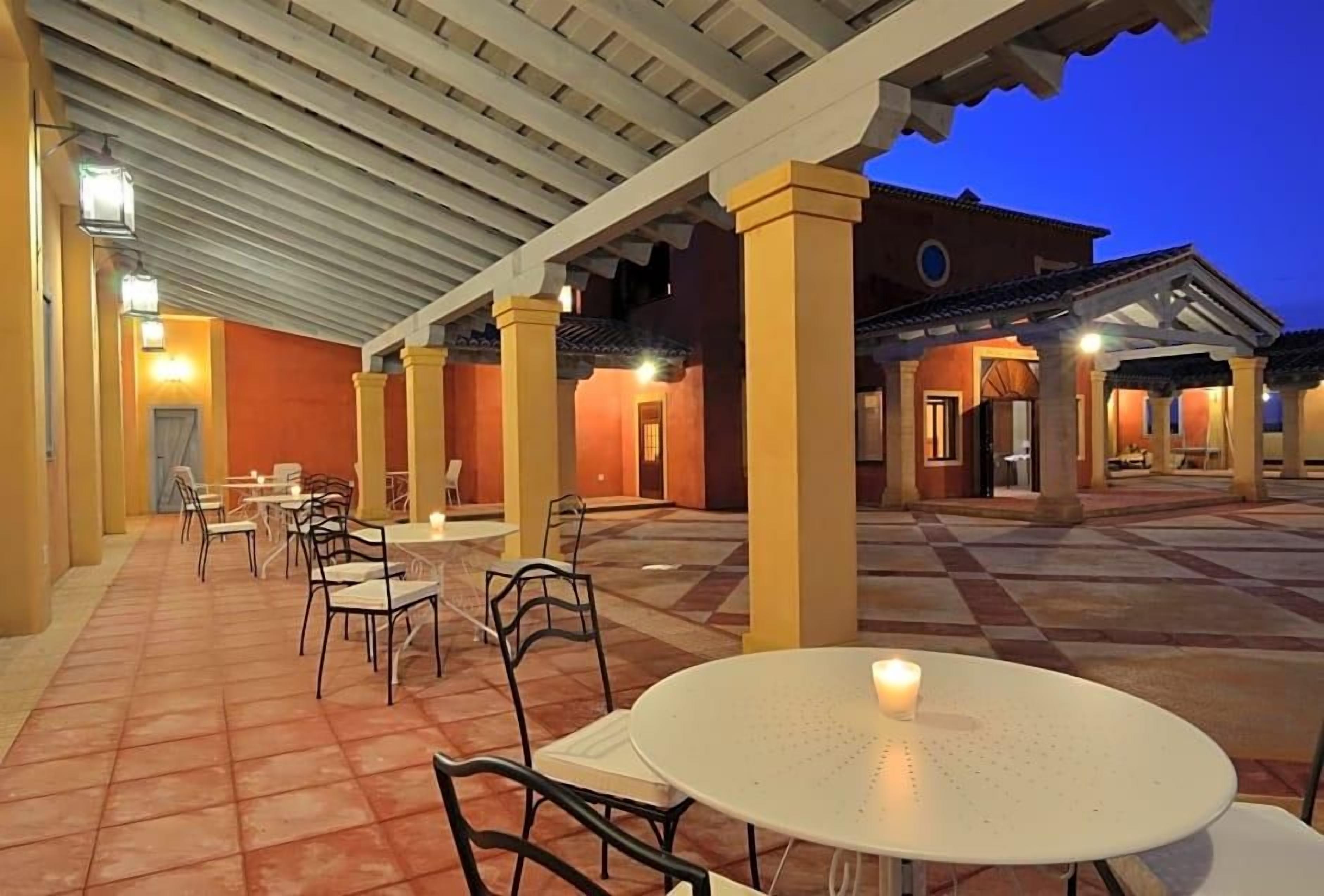 An outdoor patio area with tables and chairs, a covered walkway, and a building with a tiled roof.