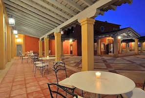 Un patio al aire libre con mesas y sillas, un corredor cubierto y un edificio con techo de tejas.