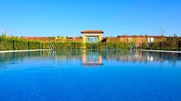 Una piscina azul cristalina con un pabellón en el centro, rodeada de follaje y edificios.