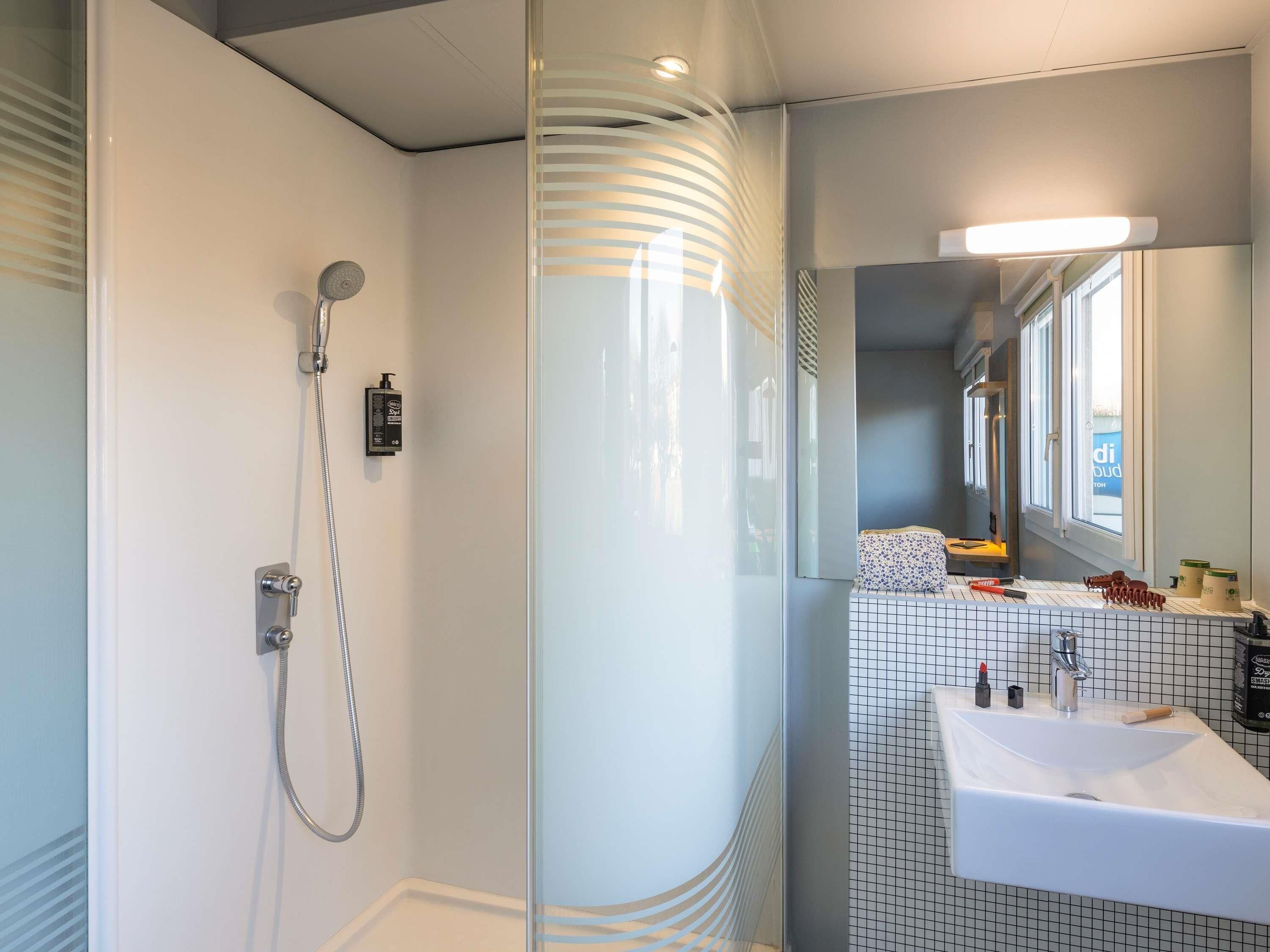 Une salle de bain moderne avec une douche à parois de verre, un lavabo blanc et un miroir au-dessus.