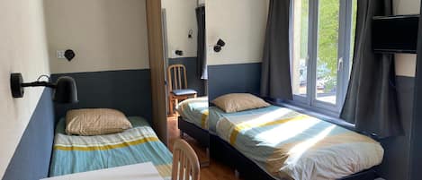 A compact room with two single beds, a table, a chair, a TV, and a window with curtains.