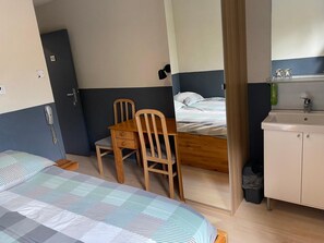 A room with a bed, a wooden table with two chairs, a small bedside table, a mirror, and a sink with cabinets. - Hotel Fauwater (Kasterlee)